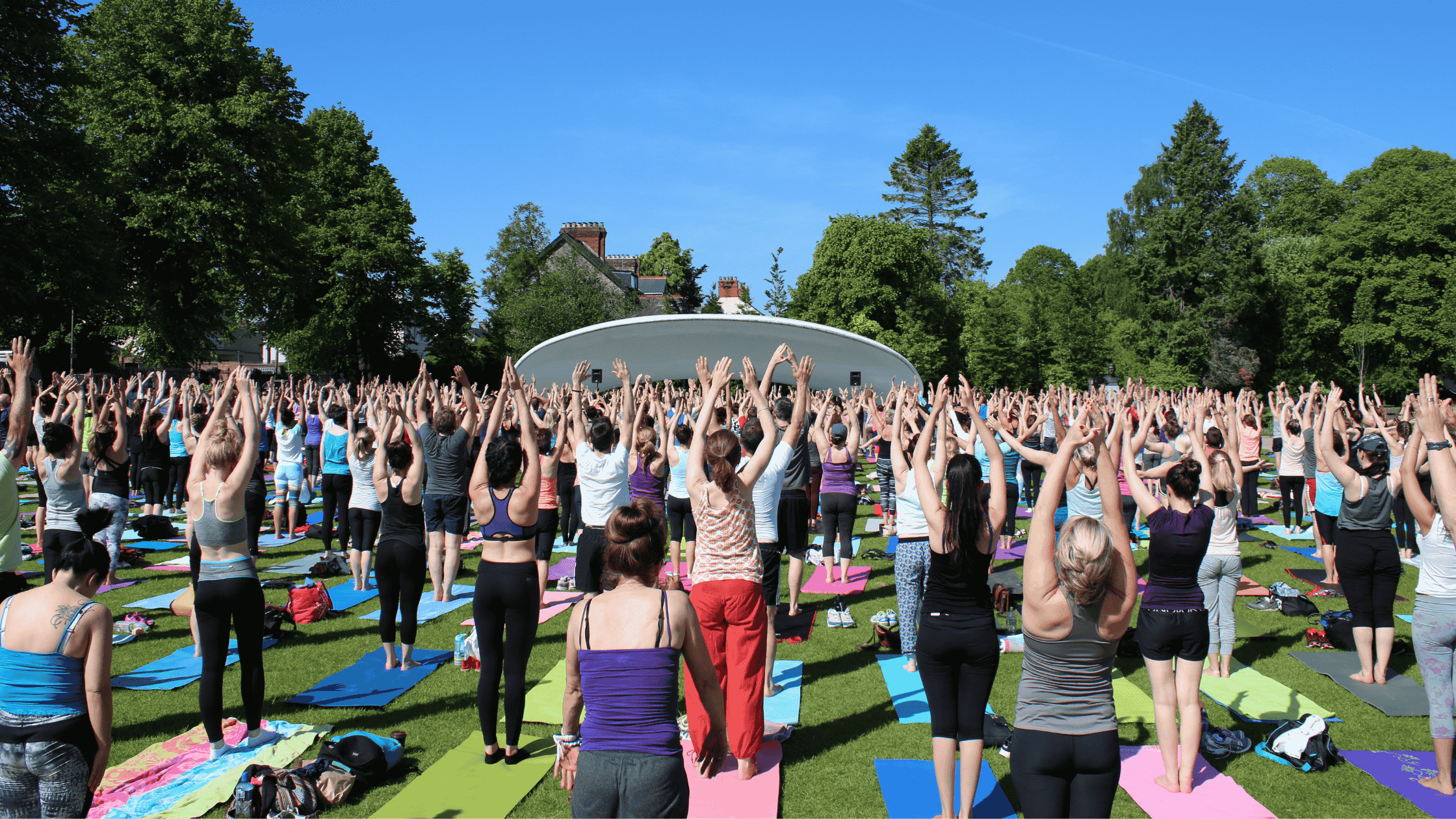 A group of people practising yoga on mats in the grass during a sunny morning class at Fitzgerald Park, Cork