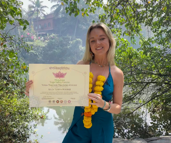 Lucy Bourke holding her Yoga Teacher Training certificate at Himalaya Yoga Valley in India
