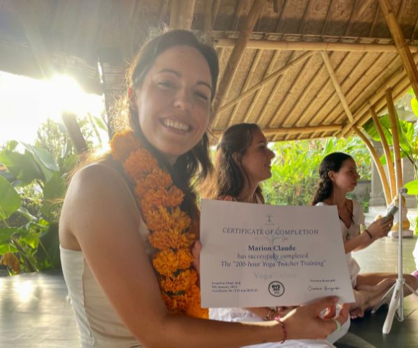 Marion Claude holding her 200-hour Yoga Teacher Training certificate at a yoga graduation