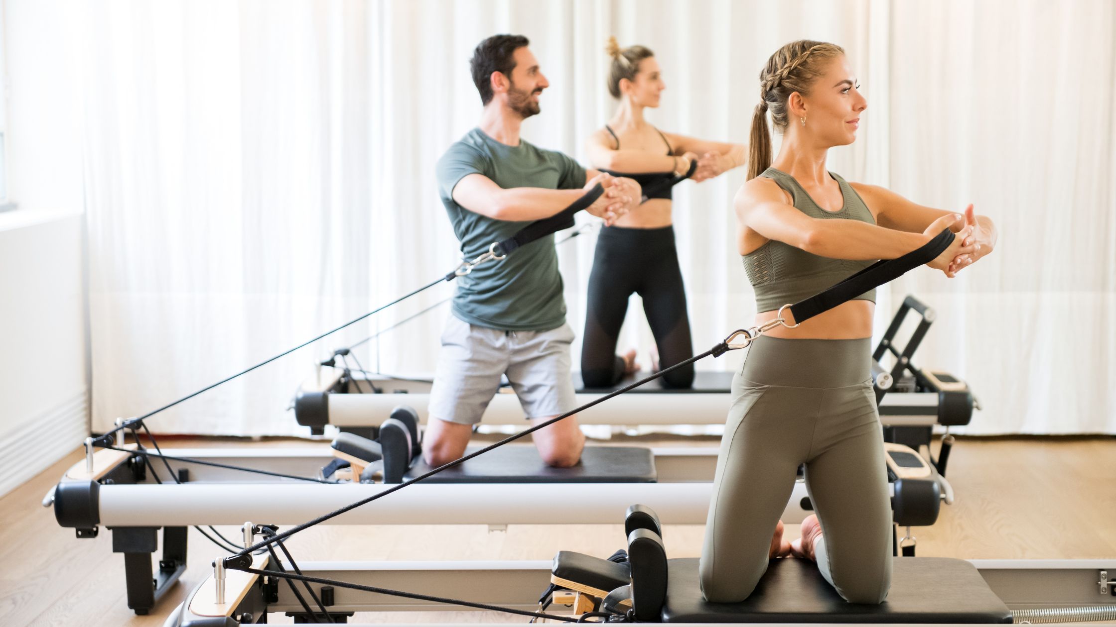three people exercising-torso rotation at a reformer pilates class